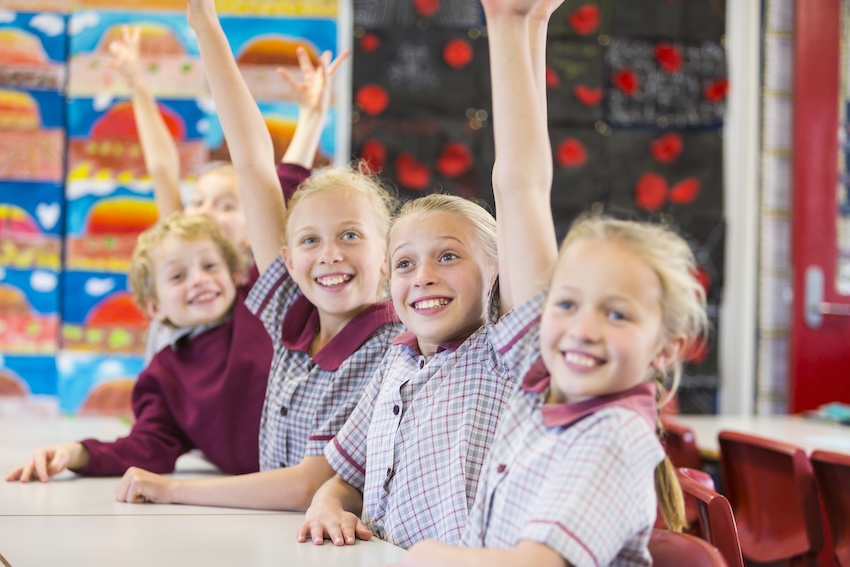 Hands Raised Smiling School Children in the Classroom Smiling young school children with their hands raised answering questions in the classroom